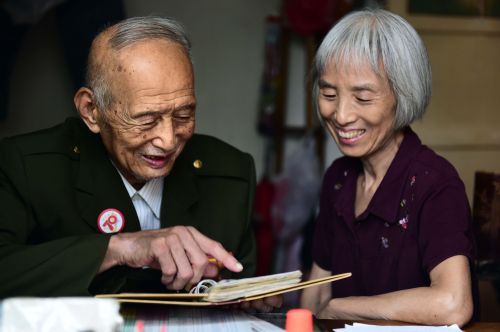 93岁抗战老兵王默村拿着相册跟女儿王慧珍讲述当年的抗战故事（8月19日摄）。