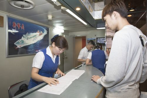  9月10日，在日本大阪&ldquo;新鑒真&rdquo;號渡輪上，工作人員（左）為登船的旅客辦手續。 